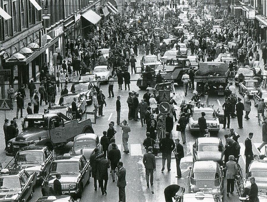 Black and white aerial photograph of a city street jammed with cars, buses and enormous crowds of onlookers.