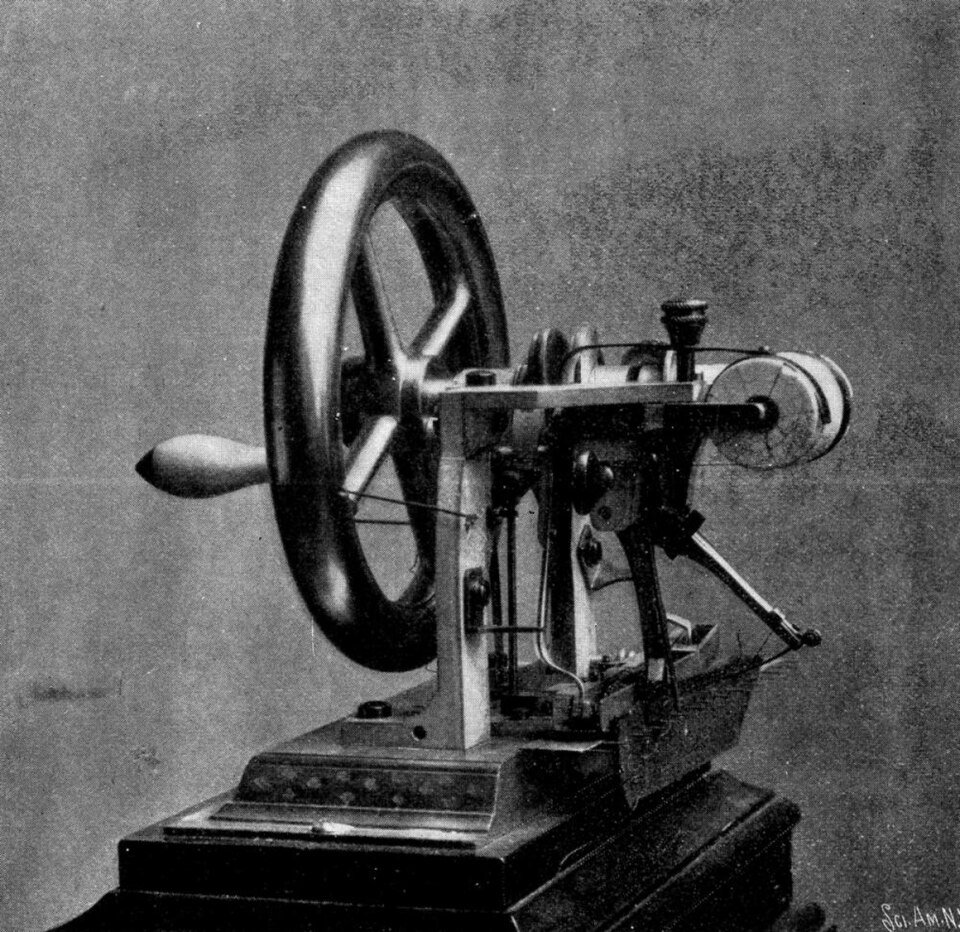 Black and white photograph of an early cast iron sewing machine with a large hand wheel.