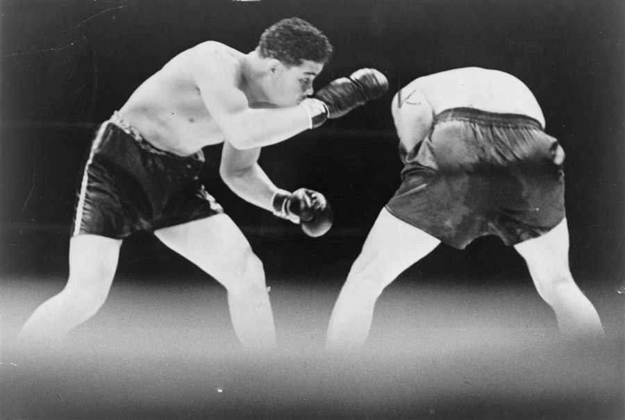 Black-and-white photograph of two boxers mid-bout, one throwing a jab while the other ducks low.