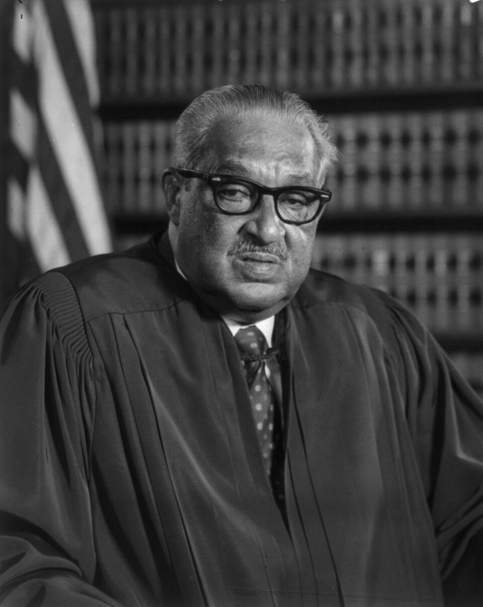 Black-and-white portrait of an older man in judicial robes and glasses, seated in front of a bookshelf.