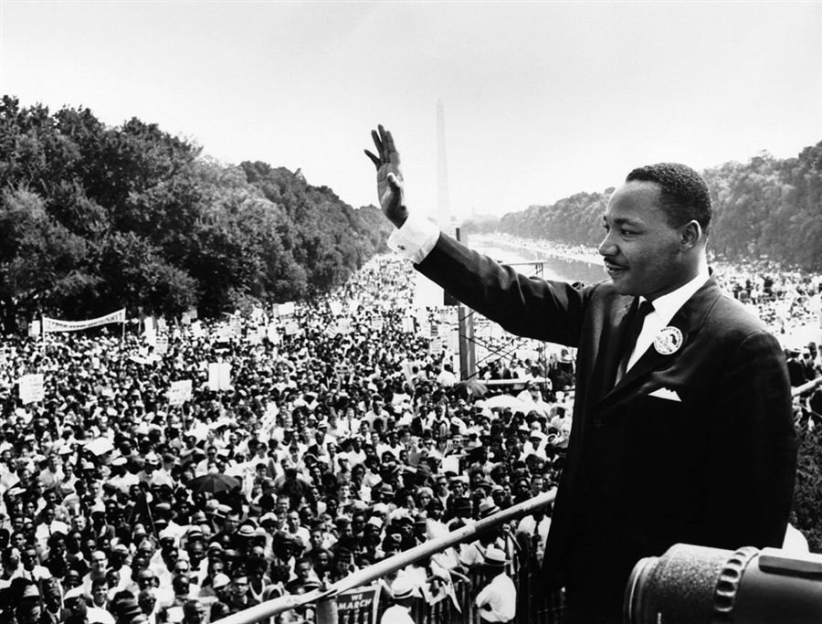 Black-and-white photograph of a man in a suit waving to an enormous crowd stretching toward a distant obelisk monument.