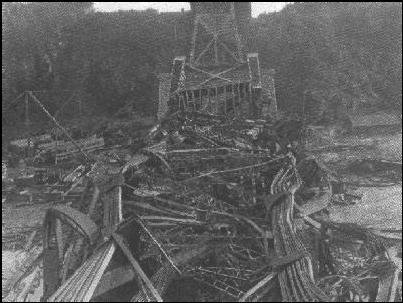 Black-and-white photograph of a massive tangled wreckage of steel girders after a bridge collapse.