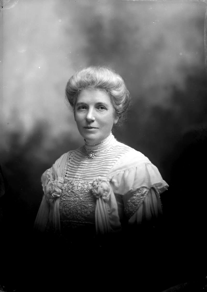 A studio photograph of a woman with swept-up grey hair in an embroidered high-necked blouse.