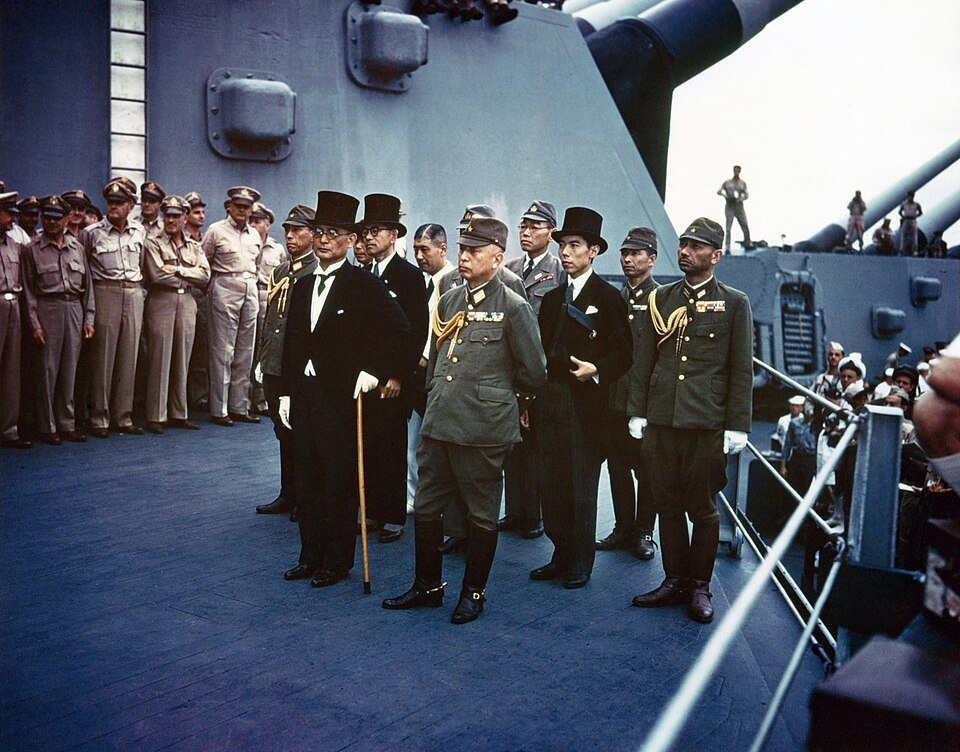 Colour photograph of Japanese officials in top hats and military uniforms standing on a battleship deck before rows of Allied officers.